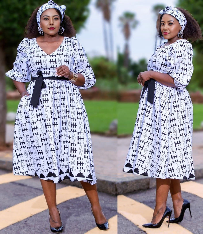 White A-line midi dress with black geometric print, V-neck, and belted waist