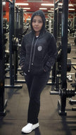Dark hooded zip tracksuit set with drawstring and round chest emblem; matching pants