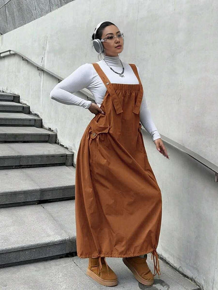 Rust-brown maxi workwear dress with adjustable straps, front pockets, and buttoned bib