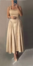 Beige pleated maxi dress with square neckline and gathered straps, flowing skirt