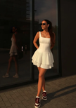 White sleeveless pleated mini dress with tiered ruffle skirt and square neckline