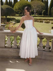 White midi dress with thin straps, fitted bodice, and flared mid-length skirt