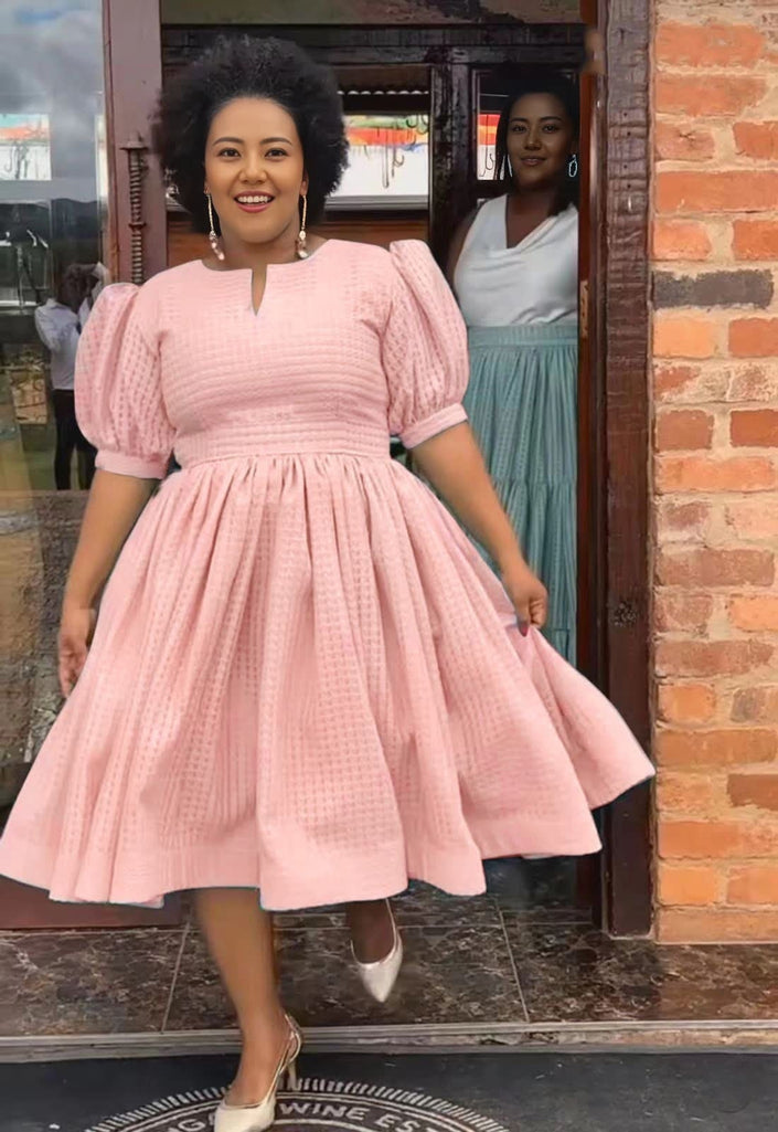 Pink textured midi dress with puff sleeves, gathered waist, and flared skirt.