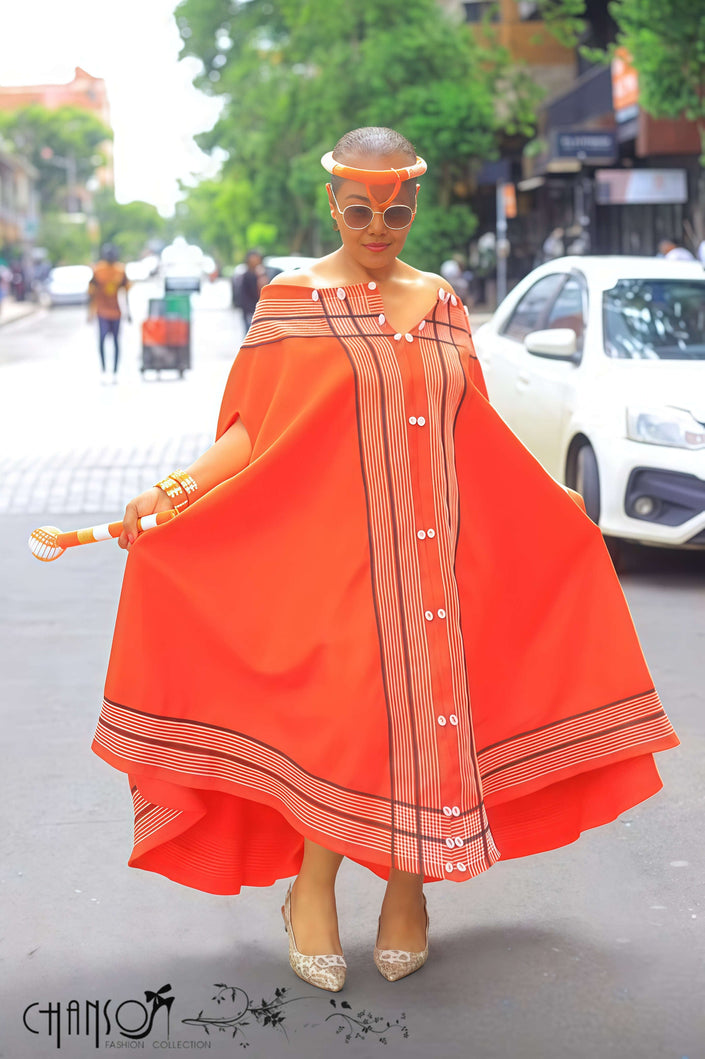Orange-red maxi dress with wide cape sleeves and striped hem border over vertical stripes