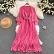 Pink pleated maxi dress with V-neck, long sleeves, and waist belt detail