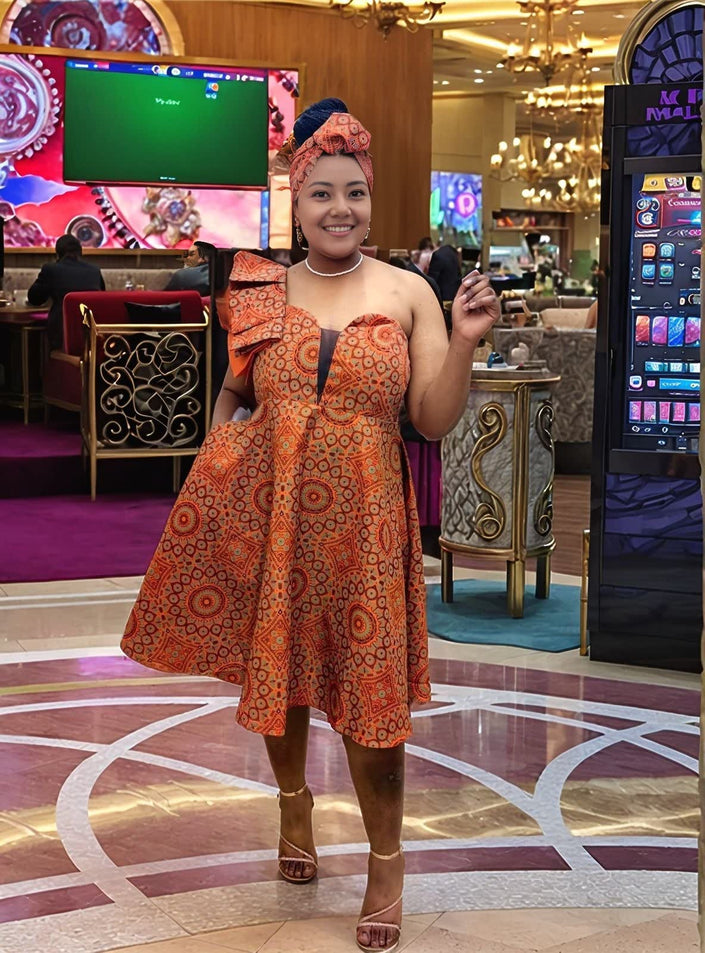 Orange-red one-shoulder midi dress with bold circular African print, ruffle shoulder