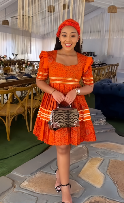 Orange traditional dress with puff sleeves, square neckline, and patterned skirt hem