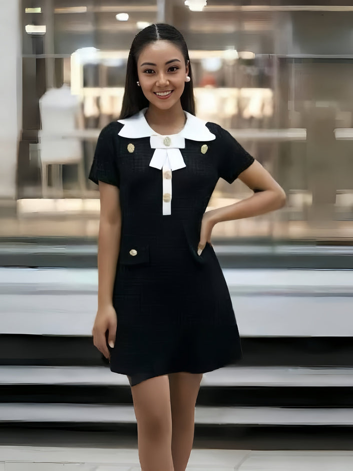 Black vintage-style dress with white collar bow and gold buttons, short sleeves