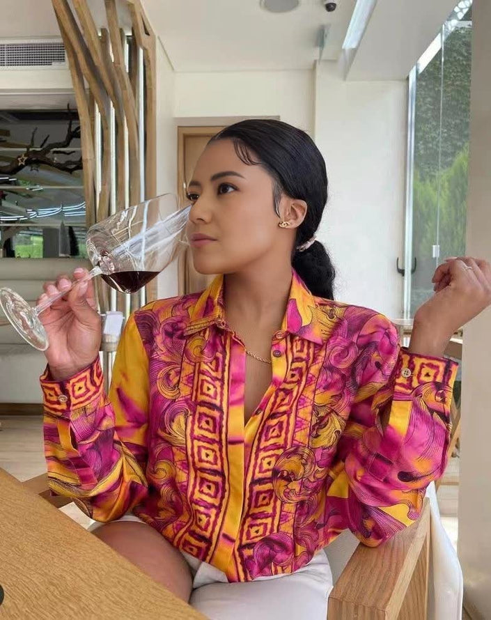 Vibrant printed long-sleeve button-up blouse with geometric swirl pattern in pink, purple, and yellow.