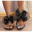 Black women's flat sandals with large sheer bow, rhinestone toe rings, and ankle chain